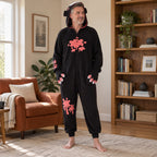 Pyjama costume chat noir aux pattes roses adulte porté de face dans un intérieur chaleureux